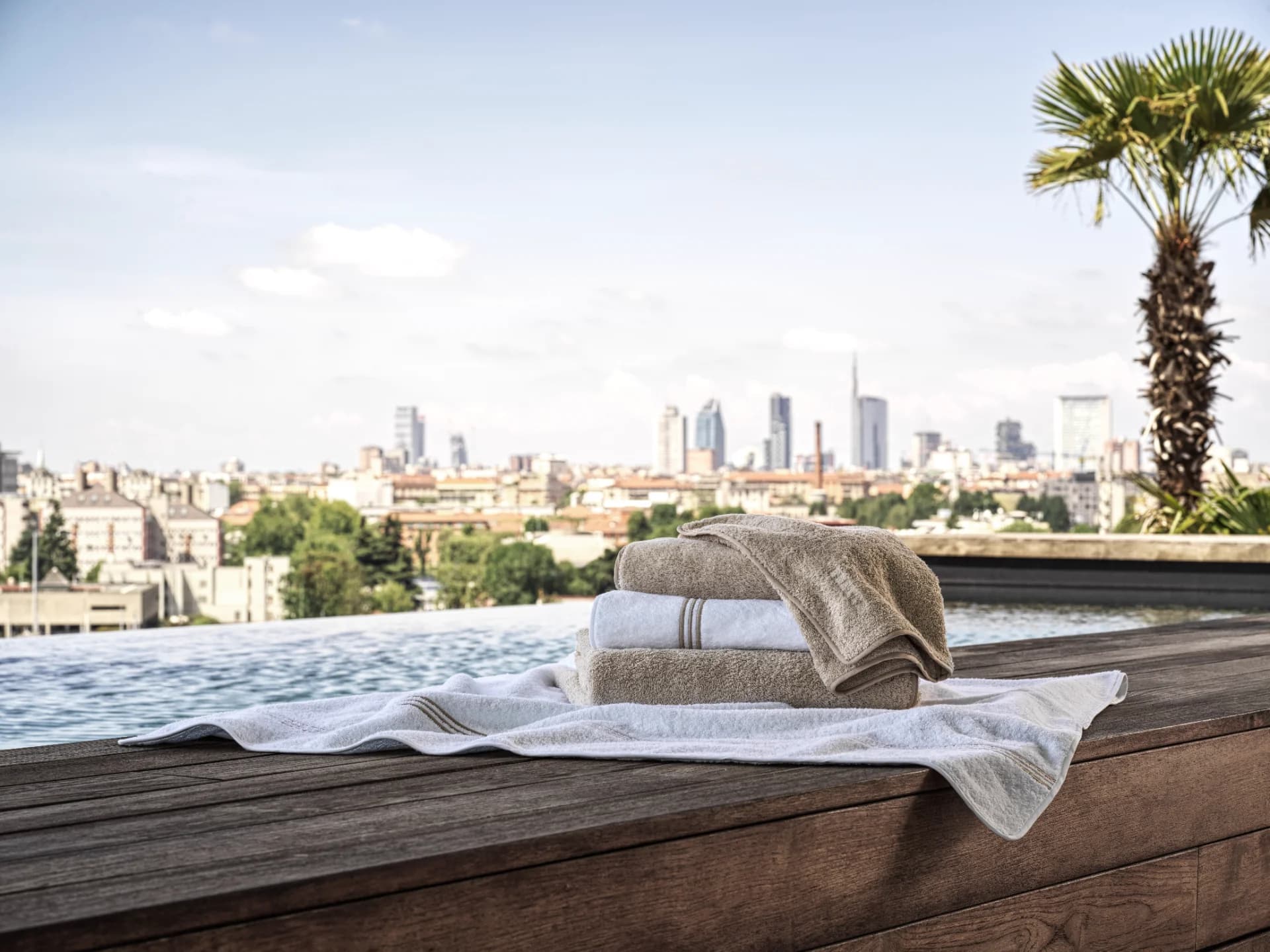 Frette Unito Towels in beige and white, folded on a pool deck with a stunning skyline view.