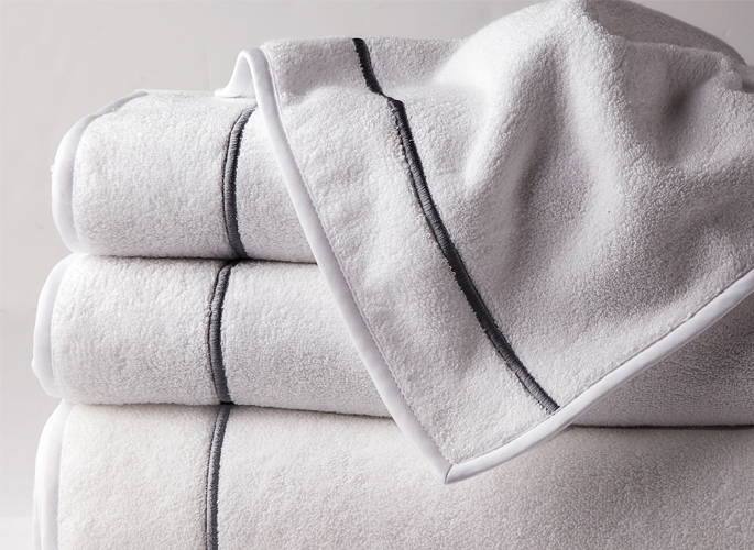 a stack of white towels with a single silver embroidered line