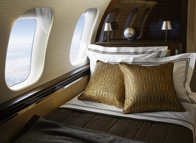 private jet bedroom with luxury gold bed linen and a view of clouds out the window