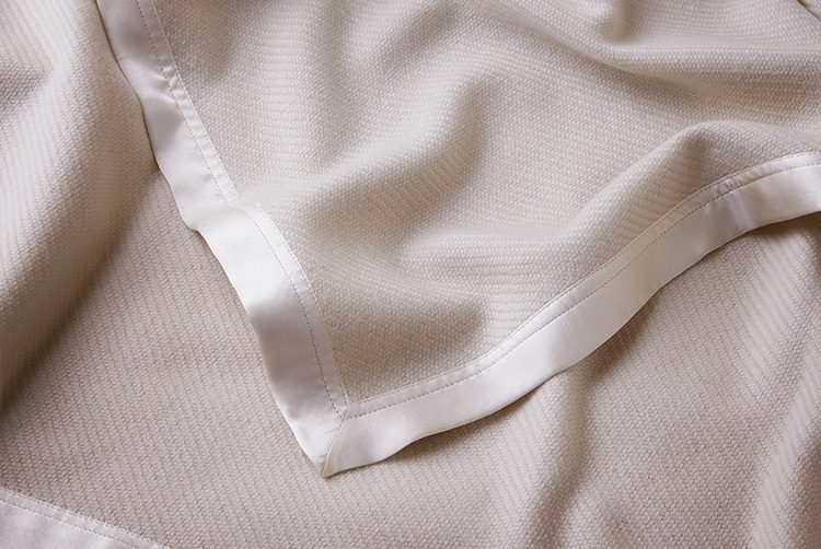 a cream cashmere throw with silk borders and a patterned weave