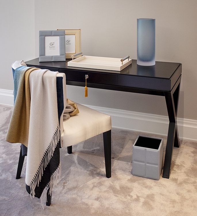 dressing table with photo frames, a trinket tray, vase and a cashmere throw hanging from the chair