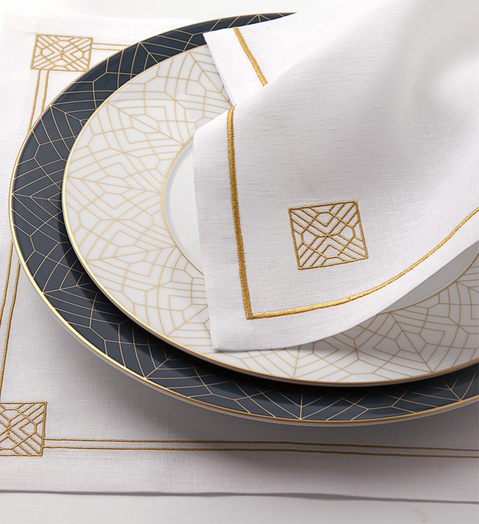 white and gold art deco patterned porcelain plate with table linen and cutlery