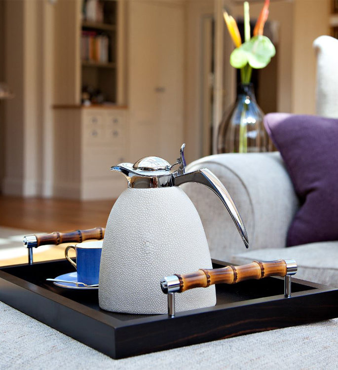 a dark wooden tray with a white leather water jug and a bright blue tea cup on top