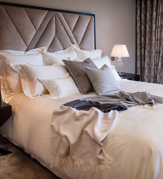 a king size bed with irory bed linen, grey cushions and a ombre blue cashmere throw