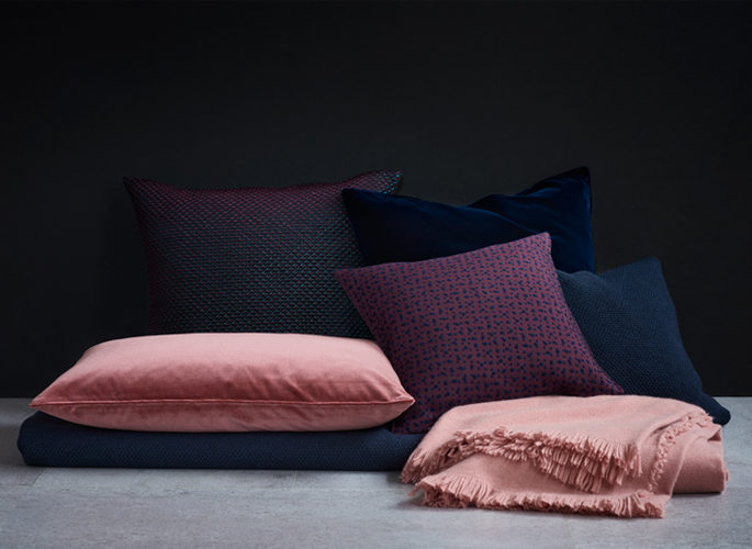 a pile of dark blue and light pink cushions lying on a dark blue cashmere throw