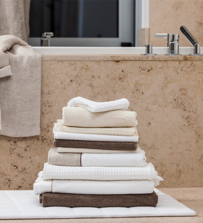a stack of neutral coloured towels next to a bath on a bathmat